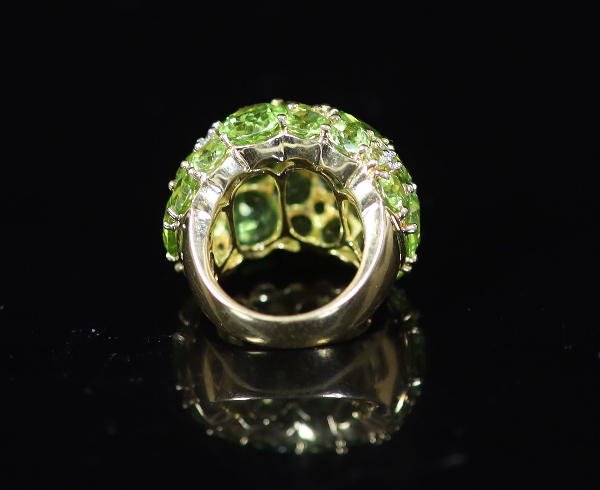 A Continental 18k gold and graduated round cut peridot encrusted dress ring, with diamond chip spacers